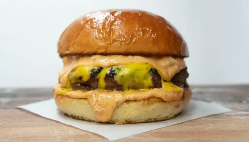 Soczysty burger z roztopionym serem i sosem na jasnym tle.